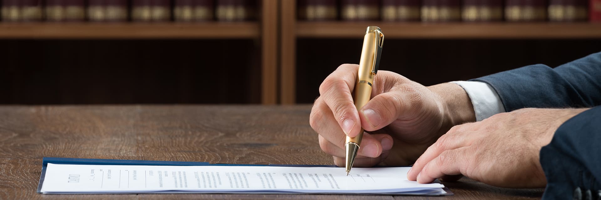 A close-up of a hand holding a pen, signing a legal document on a wooden desk.