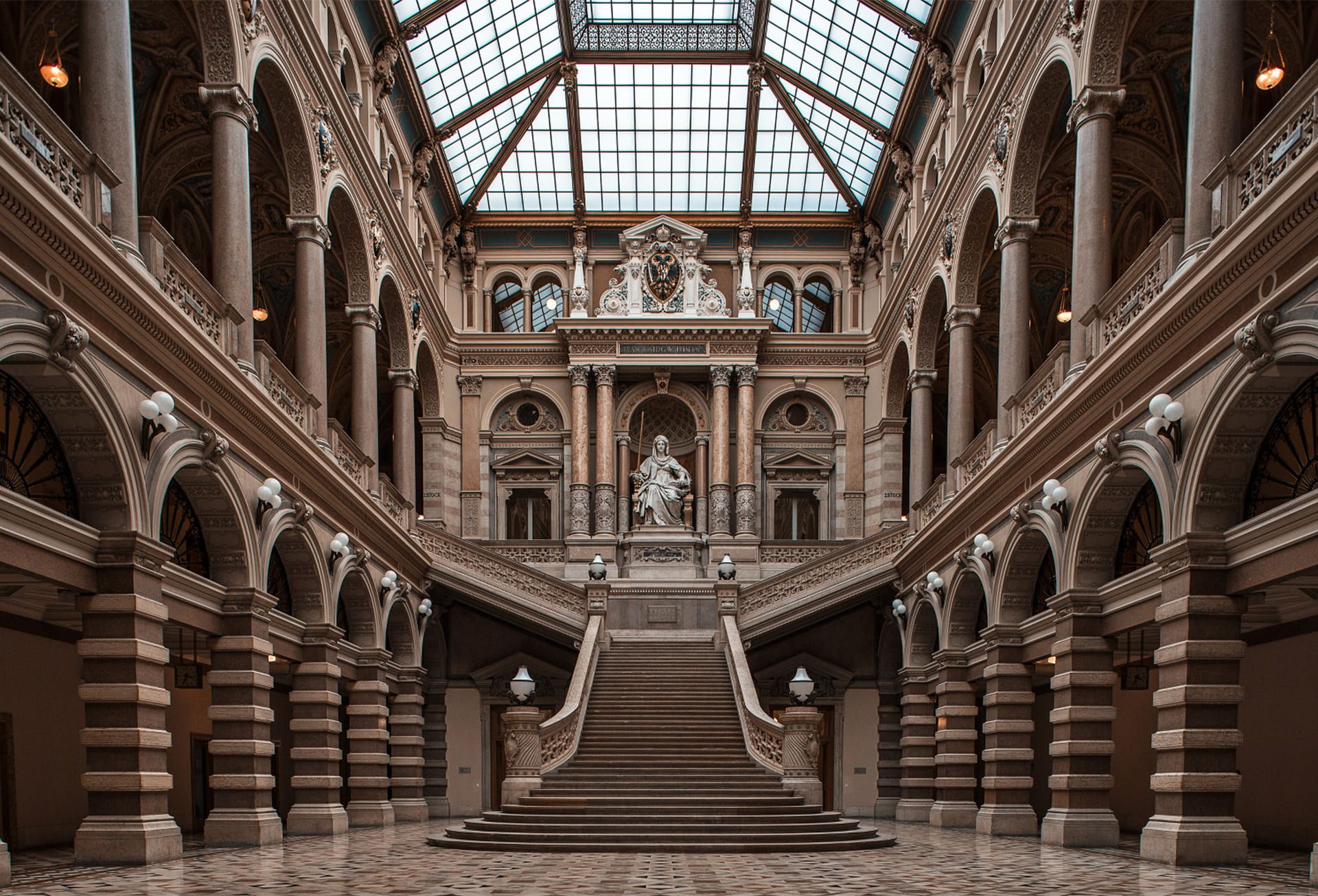A grand staircase in an ornate architectural setting with elegant columns and a glass ceiling.