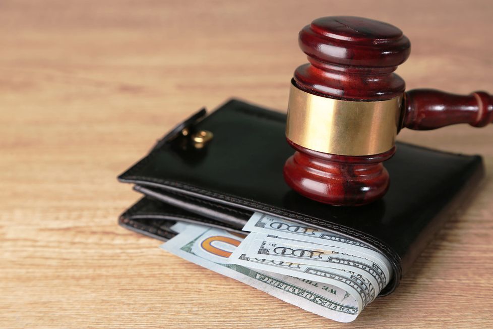 A wooden gavel resting on a black wallet with cash inside.