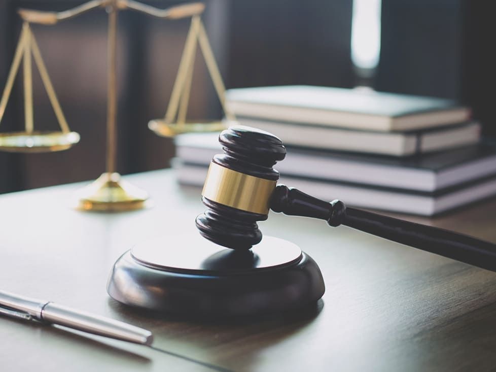 A wooden gavel resting on a desk with law books and scales.